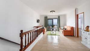 A spacious living room with a wooden staircase, a sofa, a coffee table, and a television. - Vacation Home 'Casa Ino' with Sea View, Private Terrace and Wi-Fi (Punta del Hidalgo)