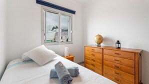 A bedroom with a bed, a wooden dresser, a globe, and a window with a view of buildings. - Vacation Home 'Casa Ino' with Sea View, Private Terrace and Wi-Fi (Punta del Hidalgo)