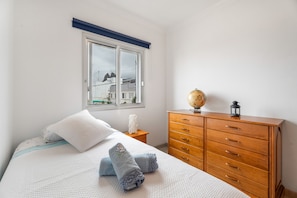 Une chambre à coucher avec un lit, une commode en bois, un globe terrestre et une fenêtre donnant sur des immeubles.