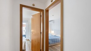 Un pasillo que conduce a un dormitorio con cama, mesita de noche y velador.