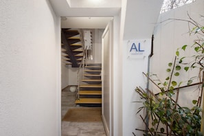 Un pasillo con una escalera, una planta y un cartel con las letras 'AL'.