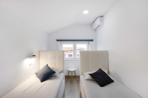 A small, modern room with two single beds, a small table, and a window with a view.