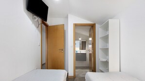 Un dormitorio con dos camas, un televisor montado en la pared y un baño visible a través de una puerta abierta.