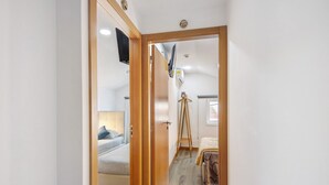 Een smalle gang die leidt naar een slaapkamer met een bed, een houten garderobe en een tv.