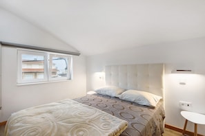 A bedroom with a bed, a window, a bedside table, and a wall-mounted light fixture.