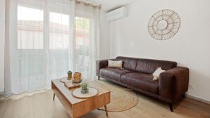 A living room with a brown leather sofa, a wooden coffee table, a glass vase, and a wall-mounted air conditioner.