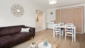 A modern living room with a brown sofa, a dining table with chairs, a white ceiling light, and a wooden door in the background.