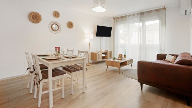 A modern living room with a dining area, a flat-screen TV, and a leather sofa.