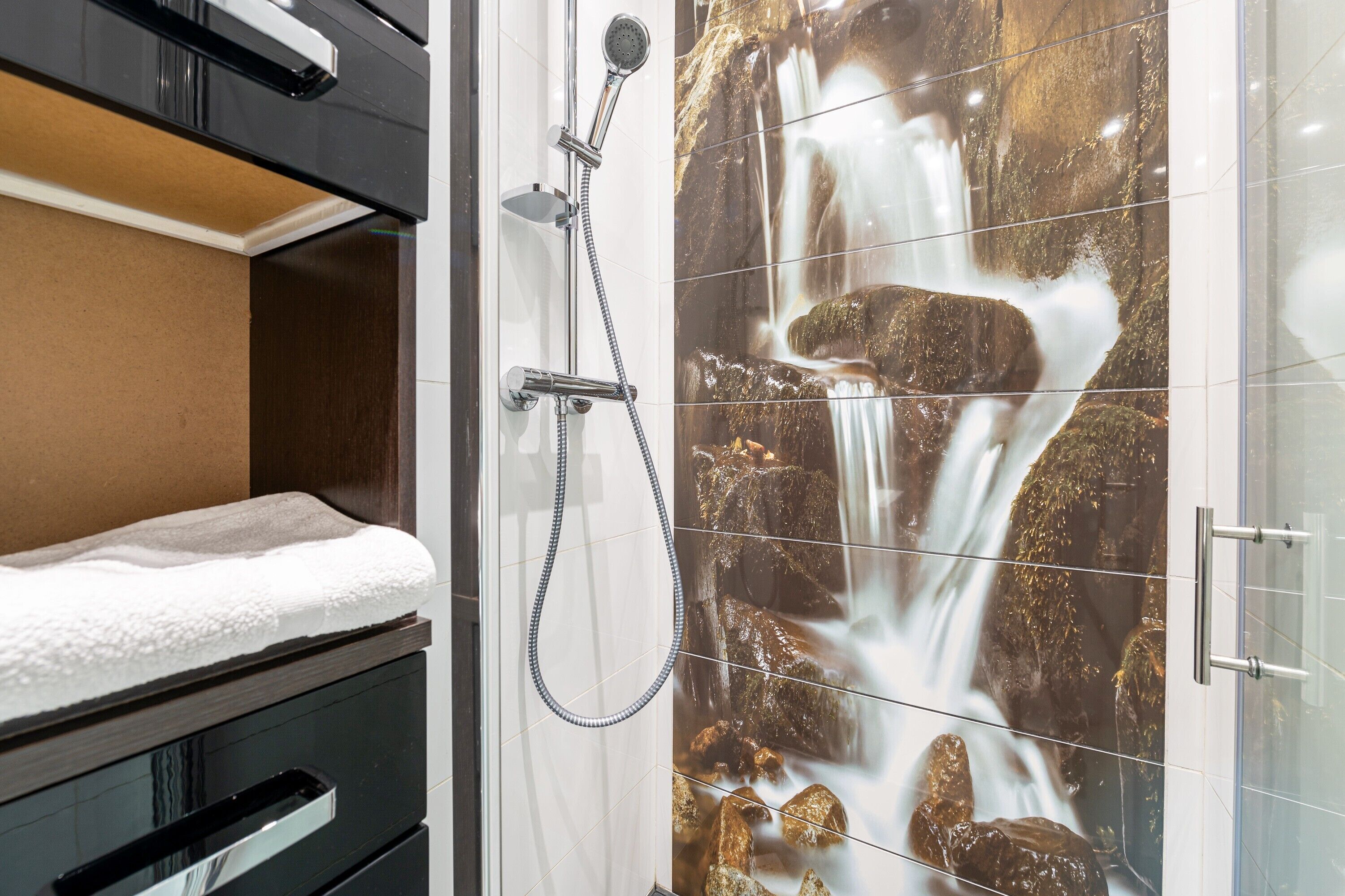 A bathroom with a shower, a towel, and a wall with a waterfall mural.