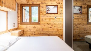 Una habitación con paneles de madera, una cama, un ventanal y dos cuadros en la pared.