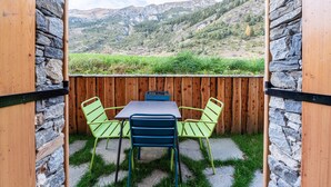 Un patio con mesa y sillas, un cerco de madera y vistas a un paisaje montañoso.