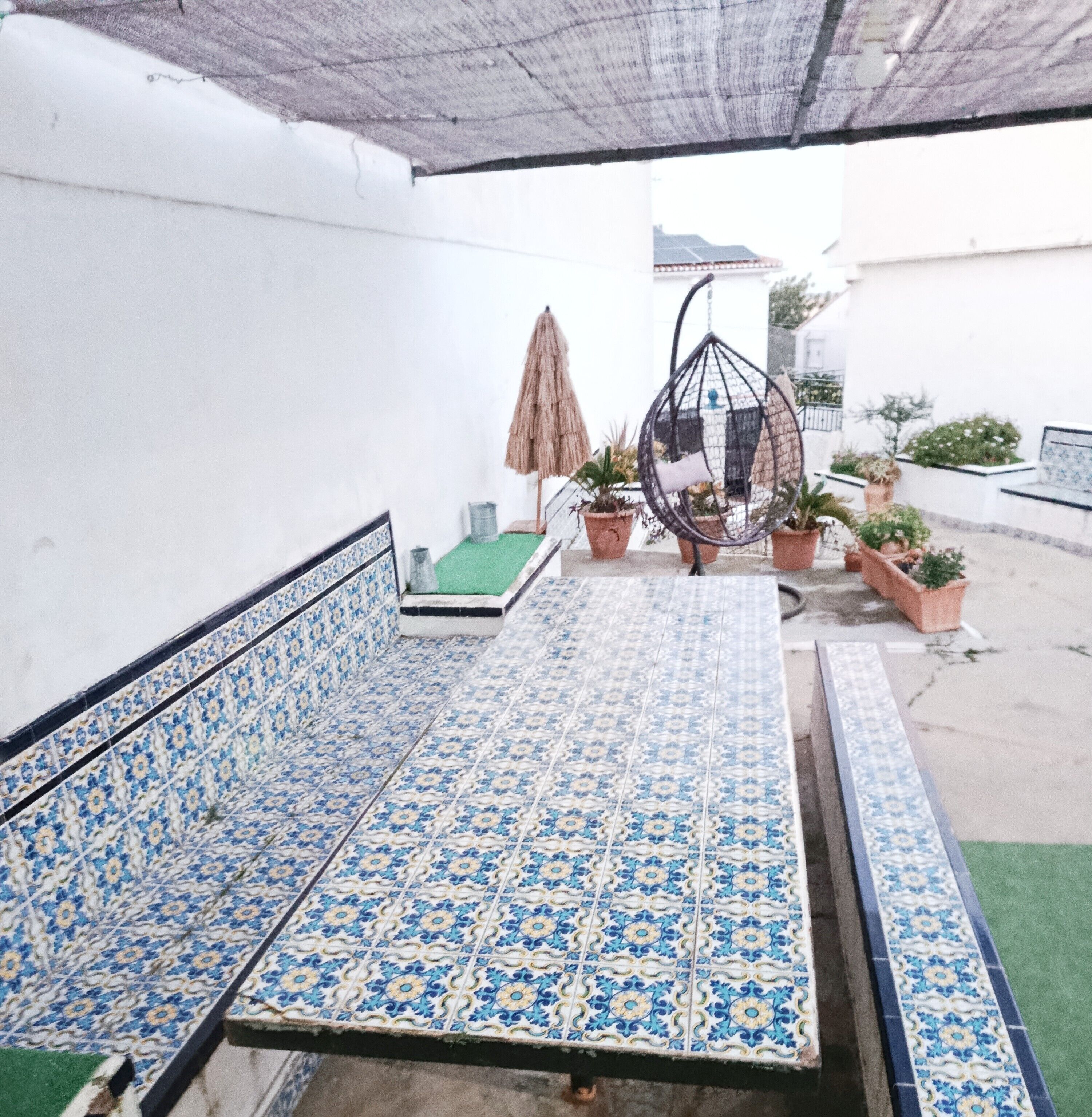 Un espace avec des bancs recouverts de carreaux, agrémenté d’une chaise suspendue et de plantes en pot.