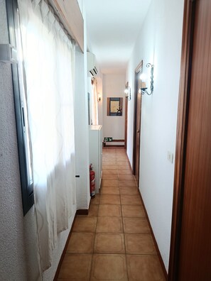 Un couloir avec un sol carrelé, un extincteur, une porte et un luminaire fixé au mur.