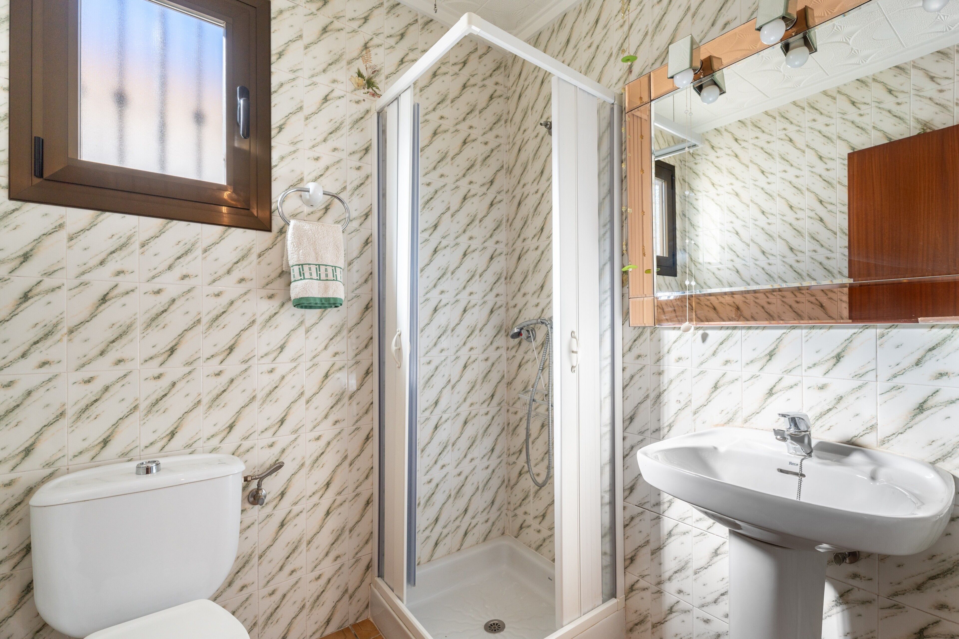 Un baño con inodoro, ducha con puerta de cristal, lavabo y espejo.