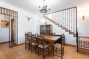 Ein Essbereich mit einem Holztisch und Stühlen, einer Treppe mit schwarzer Geländer und einer Kristallleuchter.
