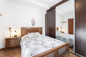 Una camera da letto con un letto in legno, un comodino, una cassettiera, uno specchio e una sveglia a parete.