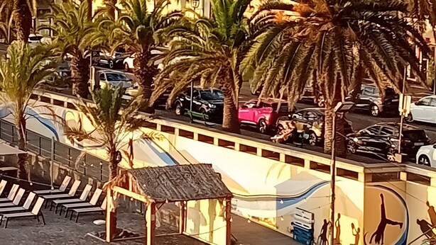 A coastal area with a church, palm trees, a parking lot, and a blue sports court.