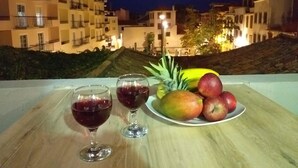 A table with two wine glasses and a plate of fruit, overlooking a cityscape at night.