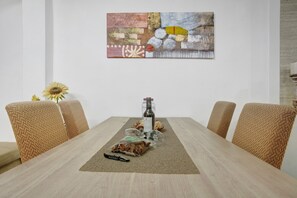 A dining table with a bottle, glasses, and bread, surrounded by woven chairs, with a painting on the wall. - Apartment 'Host Albina' with Private Terrace, Wi-Fi and Air Conditioning (Funchal)