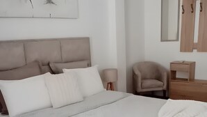 A bedroom with a large bed, a headboard, a bedside table, a chair, a mirror, and a wall-mounted light fixture.