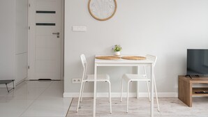 A minimalist room with a white door, a framed floral artwork, a small table with two chairs, a plant, and a TV on a wooden stand. - Warszawa Rakowska Cosy Apartment (Warszawa)