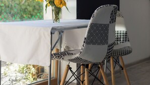 Ein Essbereich mit Tisch und Stühlen, einer Vase mit gelben Blumen und Blick durch ein Fenster.