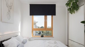 Ein ordentlich bezogenes Bett mit weißen Leinen, einem schwarzen Kopfteil und einem Fenster mit Blick auf Häuser und Bäume.