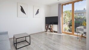 Ein geräumiges Wohnzimmer mit einem großen Schiebeglasfenster, das auf einen Balkon führt, einem Flachbildfernseher und einem Bücherregal.