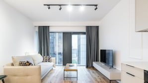 Una sala de estar moderna con un sofá, una mesa de centro, un televisor y vistas de la ciudad a través de amplios ventanales.