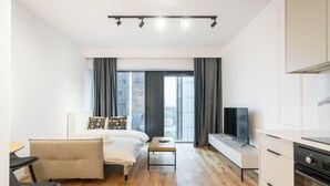 Una habitación de hotel moderna con cama, sofá, escritorio, televisor y zona de cocina.