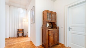 Un pasillo con piso de madera, un mueble con puertas de cristal, una silla, una lámpara y una puerta.
