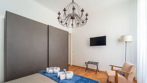 Una habitación de hotel moderna con una cama grande, televisor, una silla y una araña.