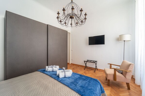 A modern hotel room with a large bed, a TV, a chair, and a chandelier.