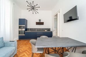 Eine moderne Küche mit Backofen, einem Esstisch mit Stühlen und einem an der Wand befestigten Flachbildfernseher.