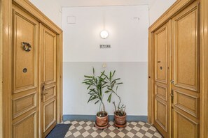 A hallway with wooden doors, a checkered floor, and two potted plants.
