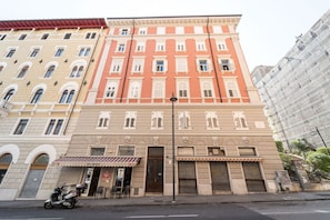 A multi-story building with a row of shops on the ground floor, a parked scooter, and a street lamp.