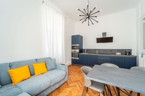 Ein modernes Wohnzimmer mit einer Couch, einem Esstisch und einer Küchenzeile mit Schränken und Geräten.