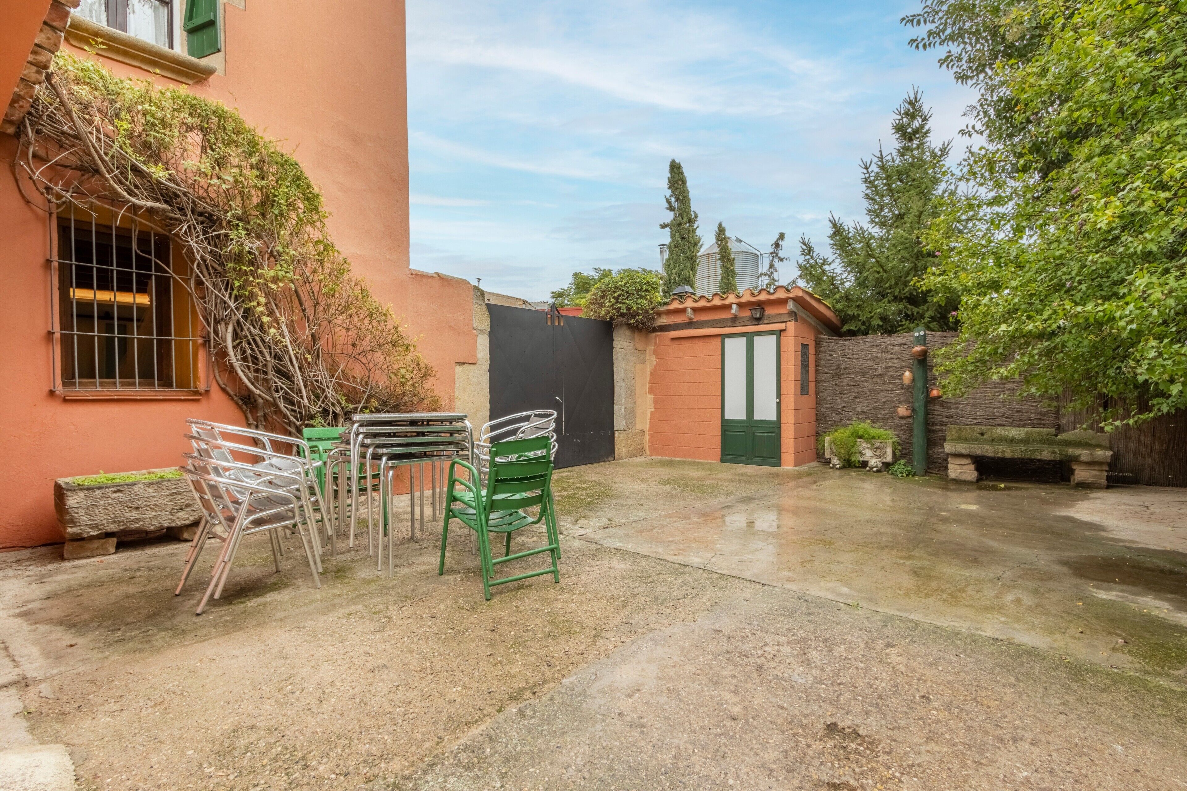 A courtyard with a table and chairs, a covered area, and a building with a door and window.