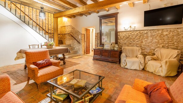 Un salon chaleureux avec un escalier, des poutres en bois, un téléviseur à écran plat et des sièges confortables.