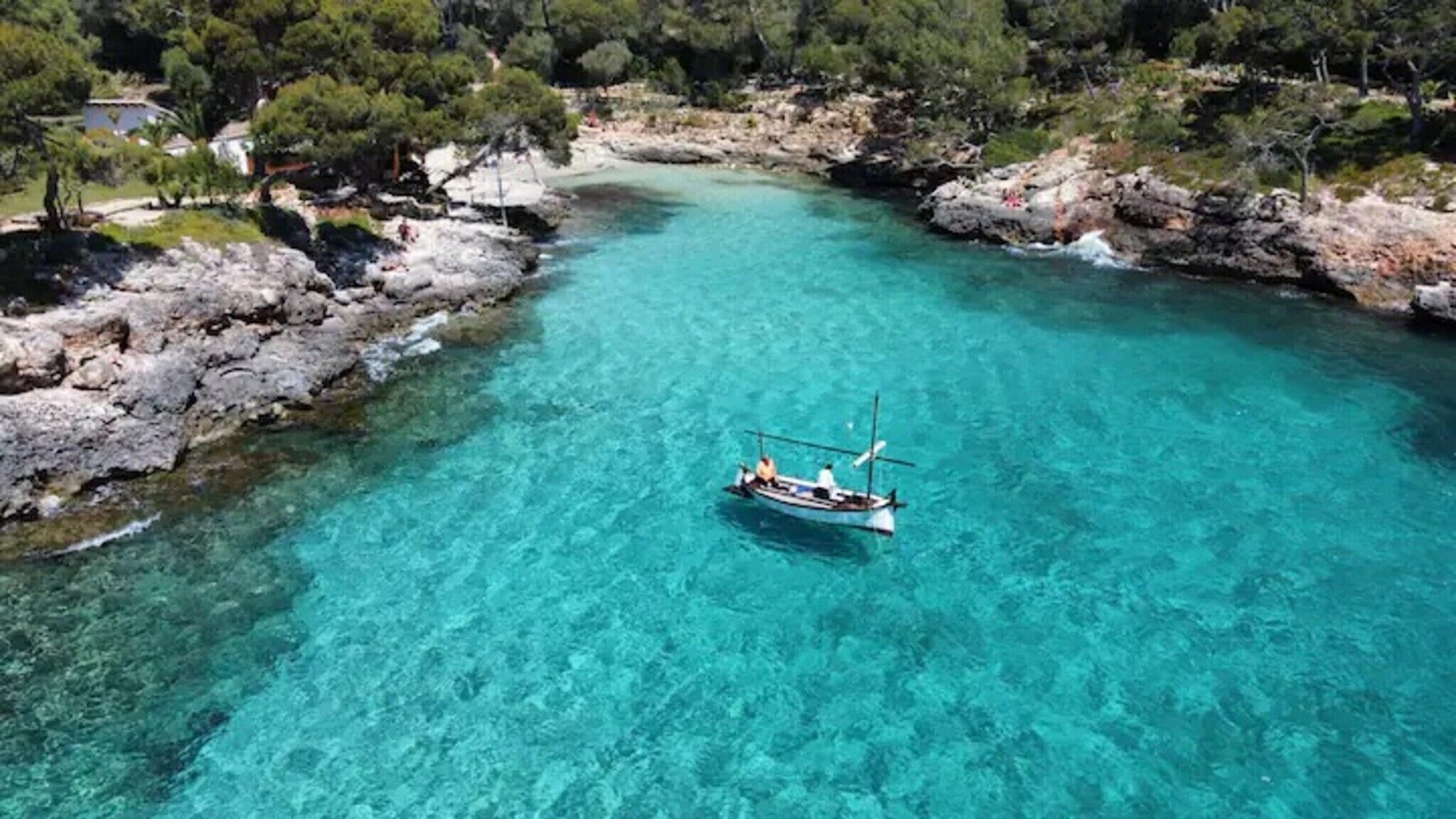 Un bateau sur une eau turquoise et limpide, entouré de côtes rocheuses et d’une végétation luxuriante.