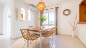 Un coin repas avec une table en bois et des chaises en osier, un luminaire suspendu et une plante en pot.