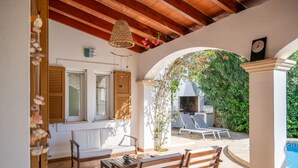 Une terrasse extérieure avec des meubles en bois, un luminaire suspendu et une vue sur une piscine.