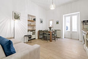 A living room with a sofa, dining table, chairs, a small side table, and a radiator.