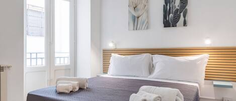 A hotel room with a bed, two pillows, a headboard, a window, and two wall art pieces.