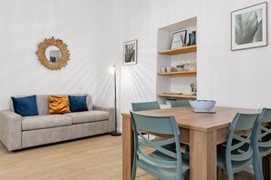 A modern living room with a sofa, a dining table with chairs, a floor lamp, and shelves with books and decorative items. - GuestHost - Cozy 61sqm apartment, for 4 people, on the 1st floor of a renovated building (NO lift and with stairs to access it). The property is located in a central area (Traffic Restricted Area), in the historic center of Palermo, a few minutes on foot (Palermo)