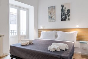 Habitación de hotel con cama, dos almohadas, cabecero, ventana y dos obras de arte en las paredes.