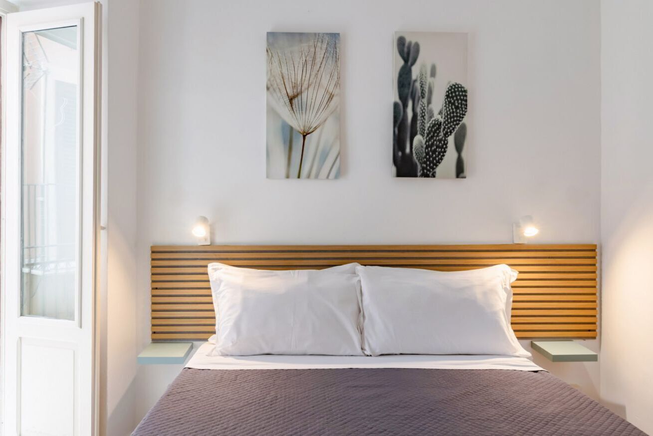 A bedroom with a wooden headboard, white bedding, two bedside tables, and wall art.