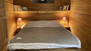 Een knus houten vertrek met een bed, twee bedlampen en een boekenkast vol boeken.