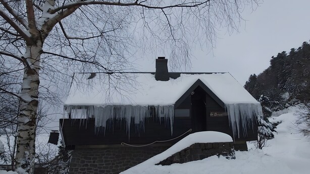 Een huis bedekt met sneeuw, met zich omlaag hangende ijspegels, een stenen fundering en een schoorsteen.