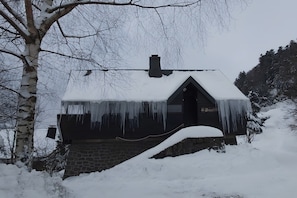 Una casa cubierta de nieve con borbotones de hielo colgando del tejado, un cimiento de piedra y una chimenea.
